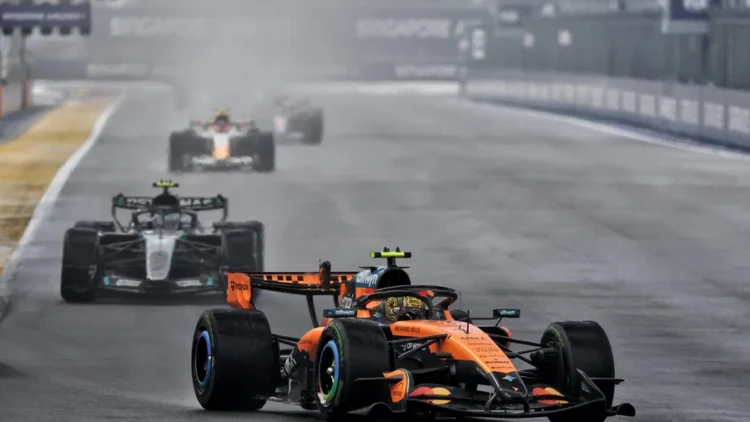 Mobil McLaren Formula 1 berwarna oranye melaju di lintasan basah, diikuti beberapa mobil lain