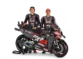 Dua pembalap berseragam Aprilia Racing berdiri di belakang motor balap RS-GP26 dengan latar putih