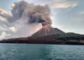 Ilustrasi gunung berapi dengan kepulan abu tebal di atas kawah, terlihat dari perairan