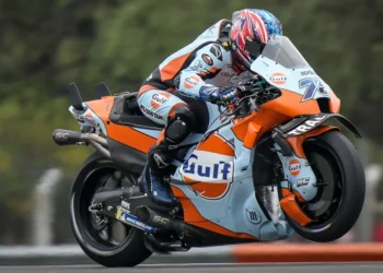 Ai Ogura mengendarai motor balap Trackhouse Aprilia berwarna oranye dan biru muda dengan livery Gulf di lintasan.