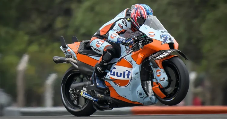 Ai Ogura mengendarai motor balap Trackhouse Aprilia berwarna oranye dan biru muda dengan livery Gulf di lintasan.