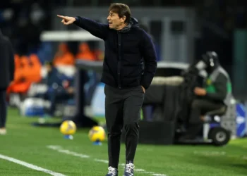 Antonio Conte mengenakan jaket gelap sambil menunjuk dengan tangan kanannya di tepi lapangan sepak bola.
