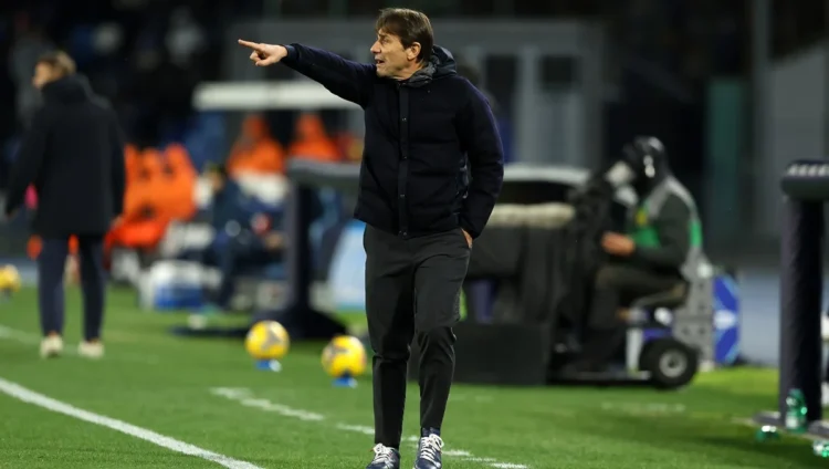 Antonio Conte mengenakan jaket gelap sambil menunjuk dengan tangan kanannya di tepi lapangan sepak bola.