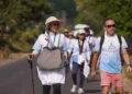 Sejumlah peserta wisata jalan kaki Camino de Flores berjalan berkelompok di jalan beraspal dengan tas, topi, dan tongkat jalan