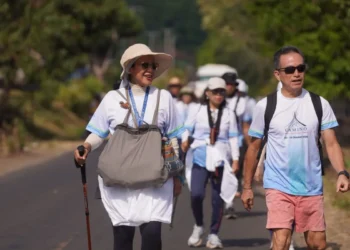 Sejumlah peserta wisata jalan kaki Camino de Flores berjalan berkelompok di jalan beraspal dengan tas, topi, dan tongkat jalan