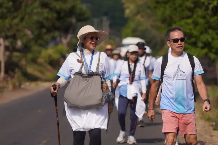 Sejumlah peserta wisata jalan kaki Camino de Flores berjalan berkelompok di jalan beraspal dengan tas, topi, dan tongkat jalan