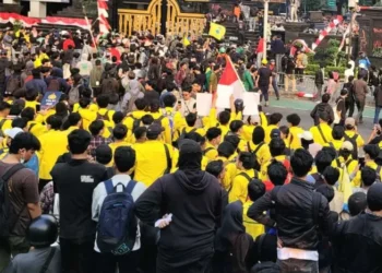 Kerumunan mahasiswa mengenakan jas almamater kuning dan peserta aksi lainnya membawa bendera di jalan