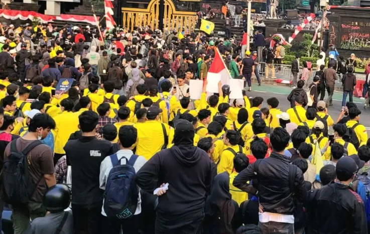 Kerumunan mahasiswa mengenakan jas almamater kuning dan peserta aksi lainnya membawa bendera di jalan