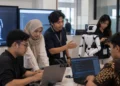 Ilustrasi beberapa pekerja menggunakan laptop dan berdiskusi dengan robot putih di sebuah ruang pengembangan teknologi