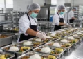 Ilustrasi petugas dapur mengenakan perlengkapan kebersihan menyiapkan porsi makanan di wadah logam