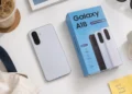 Samsung Galaxy A18 berwarna perak di samping kotak kemasan berwarna biru bertuliskan Galaxy A18, ditata di atas meja putih