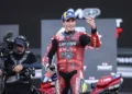 Pembalap Ducati Lenovo Team mengenakan baju balap merah dan topi biru sambil melambaikan tangan di depan kamera televisi