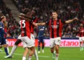 Para pemain AC Milan berseragam merah dan hitam saling berpelukan merayakan gol, dengan pemain lawan berbaju biru di lapangan