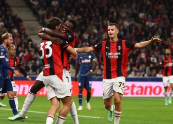 Para pemain AC Milan berseragam merah dan hitam saling berpelukan merayakan gol, dengan pemain lawan berbaju biru di lapangan