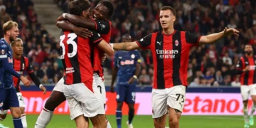 Para pemain AC Milan berseragam merah dan hitam saling berpelukan merayakan gol, dengan pemain lawan berbaju biru di lapangan