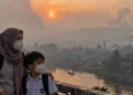 Ilustrasi seorang ibu berhijab dan anak berseragam sekolah mengenakan masker di depan permukiman yang tertutup kabut asap