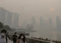 Ilustrasi warga bermasker di tepi Marina Bay dengan gedung-gedung Singapura tampak tertutup kabut tebal