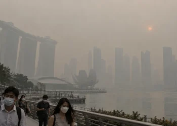 Ilustrasi warga bermasker di tepi Marina Bay dengan gedung-gedung Singapura tampak tertutup kabut tebal