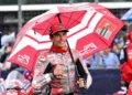 Marc Marquez mengenakan seragam Ducati merah dan memegang payung merah sambil mengacungkan ibu jari
