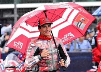 Marc Marquez mengenakan seragam Ducati merah dan memegang payung merah sambil mengacungkan ibu jari