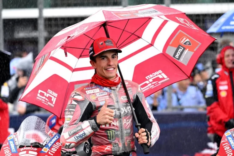 Marc Marquez mengenakan seragam Ducati merah dan memegang payung merah sambil mengacungkan ibu jari