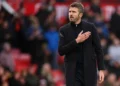 Michael Carrick mengenakan mantel hitam di sisi lapangan sepak bola