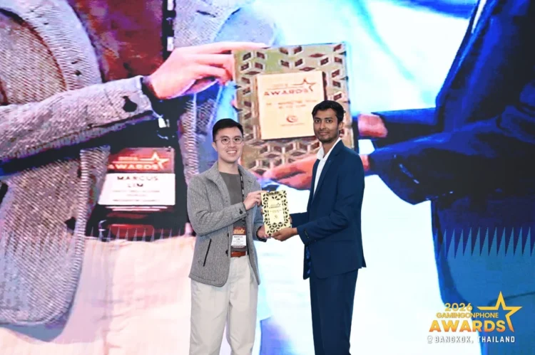 Dua orang berdiri di panggung sambil memegang plakat GamingonPhone Awards 2026, dengan layar acara penghargaan di belakangnya