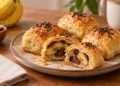 Pisang bolen panggang berwarna keemasan di atas piring, dengan potongan yang memperlihatkan isian pisang dan cokelat