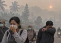 Warga dewasa berjalan di jalan berkabut asap, sebagian memakai masker dan seorang pria menutup hidung dengan lengan