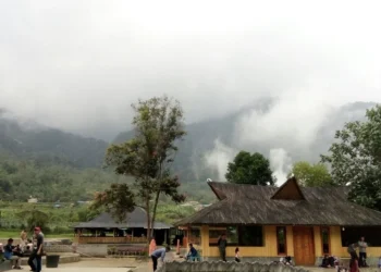 Bangunan pemandian dan pengunjung di kawasan pegunungan yang berkabut dengan pepohonan di sekitarnya