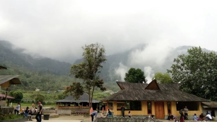 Bangunan pemandian dan pengunjung di kawasan pegunungan yang berkabut dengan pepohonan di sekitarnya