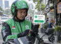 Ilustrasi pengemudi berhelm dan berjaket Gojek melihat telepon genggam di atas sepeda motor, dengan grafis notifikasi pesanan