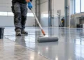 Pekerja mengaplikasikan pelapis epoxy pada lantai beton