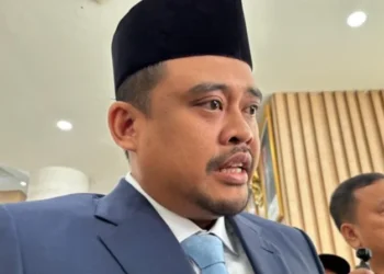 Gubernur Sumatera Utara Bobby Nasution mengenakan peci hitam, jas biru, dan dasi biru muda saat memberikan keterangan
