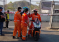 Beberapa petugas berseragam oranye berdiri di dekat skuter operasional di samping pagar area sirkuit
