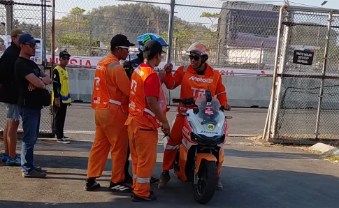 Beberapa petugas berseragam oranye berdiri di dekat skuter operasional di samping pagar area sirkuit