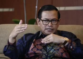 Pramono Anung mengenakan kacamata dan kemeja batik sambil berbicara dengan tangan terangkat saat duduk di kursi