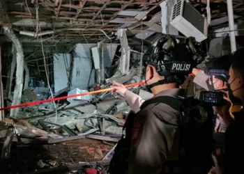 Petugas polisi memakai helm memeriksa puing dan rangka bangunan yang rusak di lokasi ledakan Pasar Cimanggis