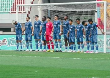 Para pemain Arema FC mengenakan seragam biru dan berbaris di depan gawang bersama penjaga gawang berseragam merah.