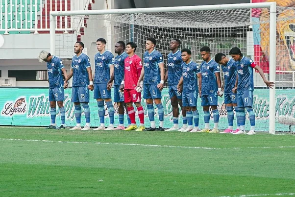 Para pemain Arema FC mengenakan seragam biru dan berbaris di depan gawang bersama penjaga gawang berseragam merah.