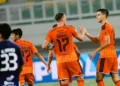 Pemain Persija Jakarta berseragam oranye saling menepukkan tangan di lapangan; pemain bernomor punggung 17 terlihat memegang bola.
