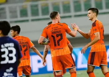 Pemain Persija Jakarta berseragam oranye saling menepukkan tangan di lapangan; pemain bernomor punggung 17 terlihat memegang bola.