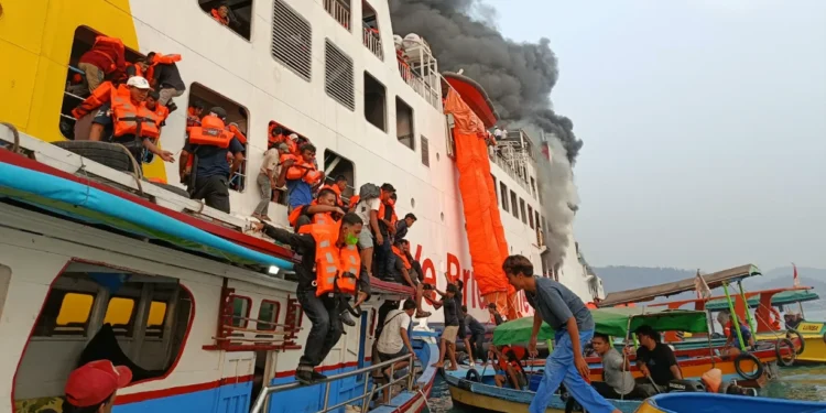 Penumpang berpelampung oranye dipindahkan dari kapal penyeberangan berasap ke perahu-perahu kecil di laut