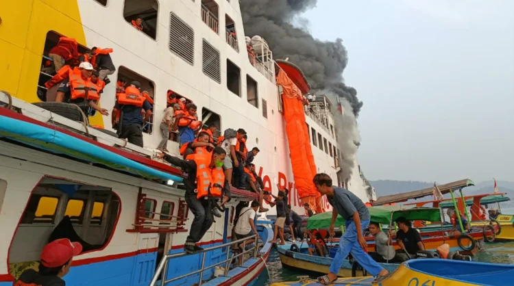 Penumpang berpelampung oranye dipindahkan dari kapal penyeberangan berasap ke perahu-perahu kecil di laut