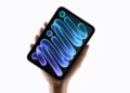 Tablet iPad mini berwarna hitam dalam genggaman tangan dengan tampilan grafis biru dan ungu pada layar