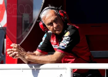 Davide Tardozzi mengenakan headset tim Ducati dan bersandar di pembatas garasi