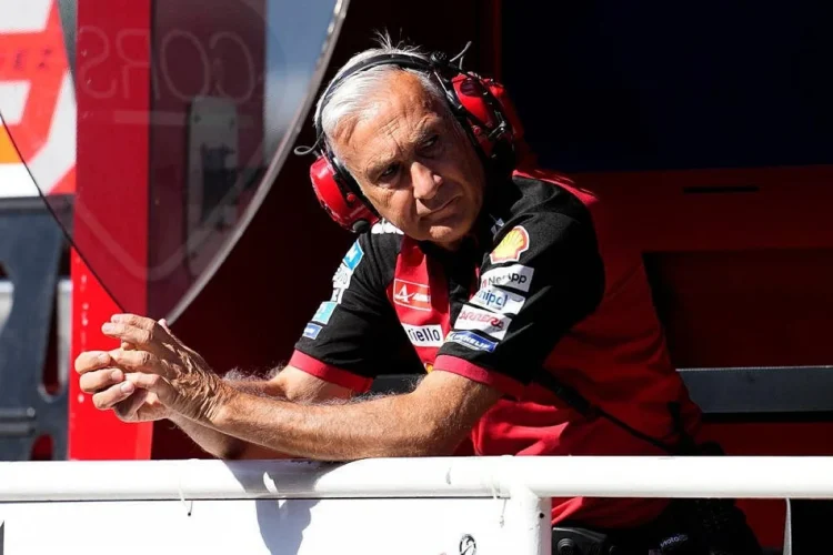 Davide Tardozzi mengenakan headset tim Ducati dan bersandar di pembatas garasi