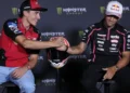 Marc Marquez mengenakan kemeja Ducati merah berjabat tangan dengan Jorge Martin berbaju tim Aprilia hitam, dengan helm di antara mereka