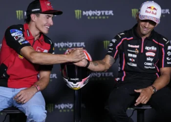 Marc Marquez mengenakan kemeja Ducati merah berjabat tangan dengan Jorge Martin berbaju tim Aprilia hitam, dengan helm di antara mereka