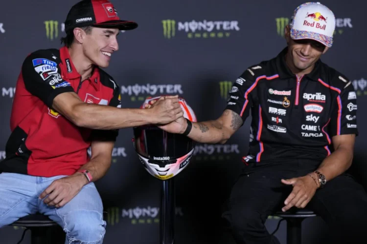 Marc Marquez mengenakan kemeja Ducati merah berjabat tangan dengan Jorge Martin berbaju tim Aprilia hitam, dengan helm di antara mereka
